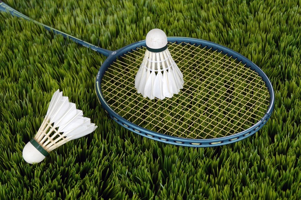 A shuttlecock resting on a racket laid down on the grass